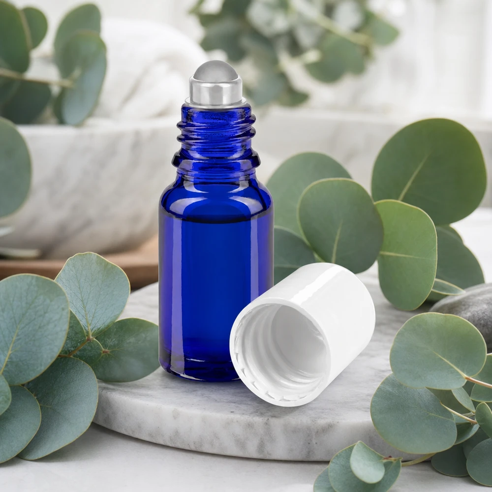 10ml blaue Roll-On Glasflasche geöffnet auf Marmorplatte umgeben von frischen Eukalyptuszweigen