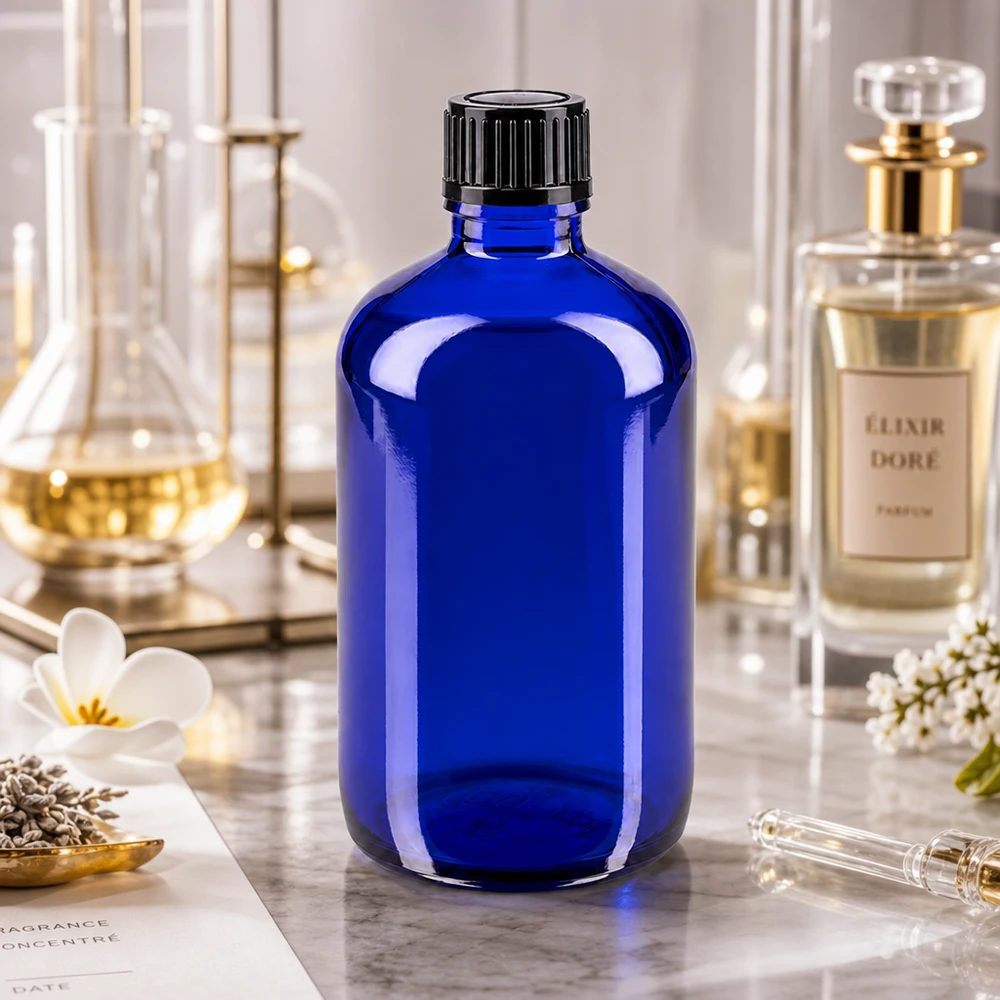 Apothekenflasche blau 100ml Schraubverschluss schwarz Standard Kobaltblaue 100ml Apothekerflasche neben Elixir Dore Parfümflakon auf Marmorunterlage