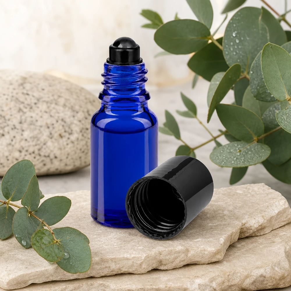 Kobaltblaue Roll-On Glasflasche 10ml mit Edelstahlkugel zwischen Steinen und frischen Eukalyptusblättern