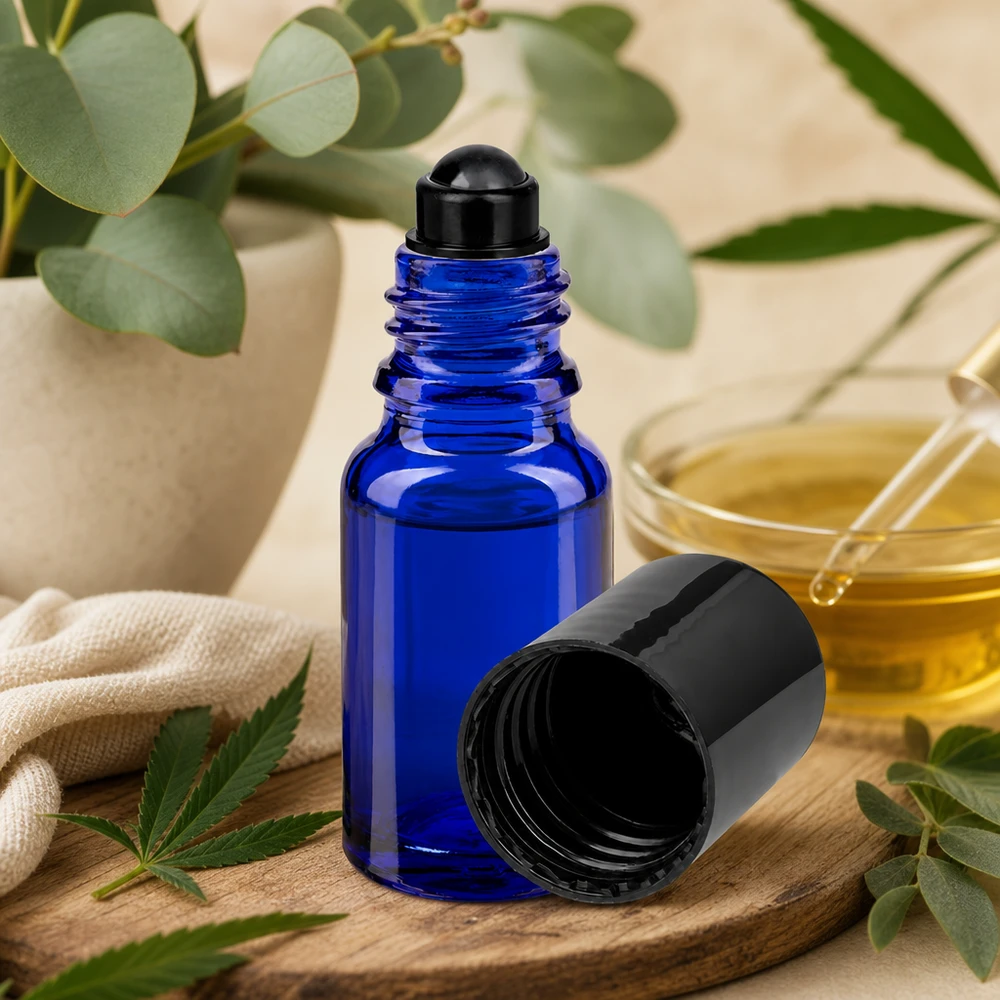 Kobaltblaue Roll-On Flasche 10ml neben goldfarbenem Öl in Glasschale und botanischen Pflanzen