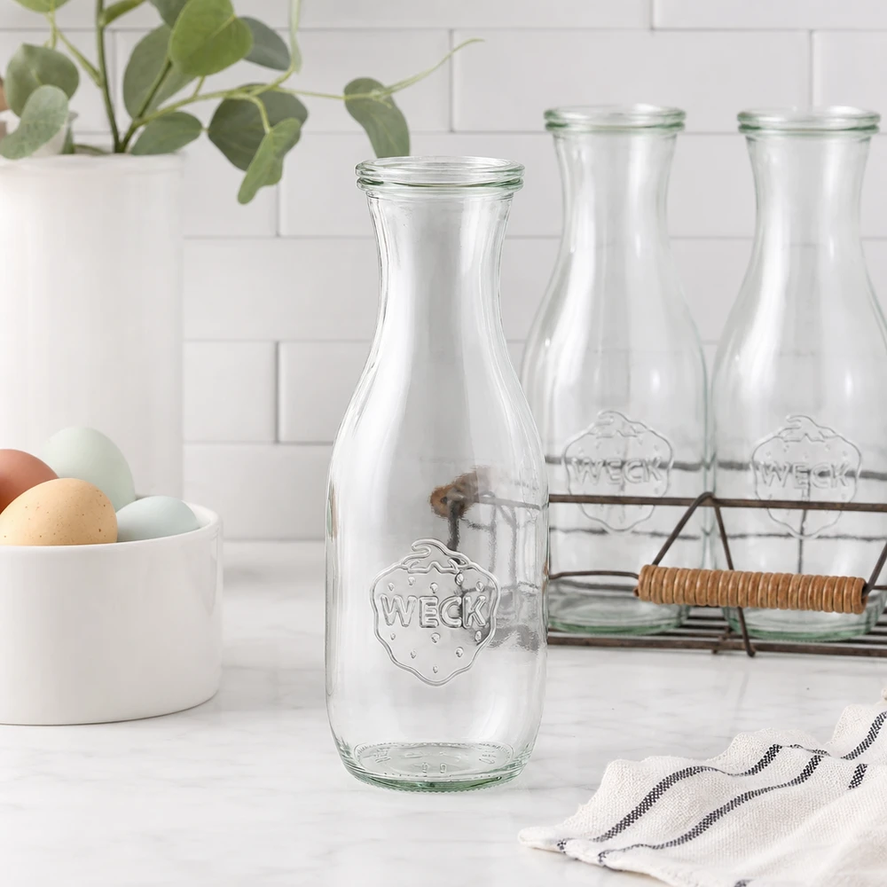 1062ml Saftflasche mit Glasdeckel WECK RR60 WECK Saftflasche 1062ml Glasflasche leer in moderner weißer Küche mit Eierschale Drahtkorb und Pflanze