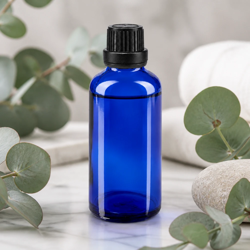 Apothekenflasche blau 50ml Tropfverschluss Giessring 2mm schwarz Originalitätsverschluss Blaue Glasflasche 50ml mit 2mm Tropfeinsatz auf Marmoroberfläche mit Natursteinen und Grünpflanzen