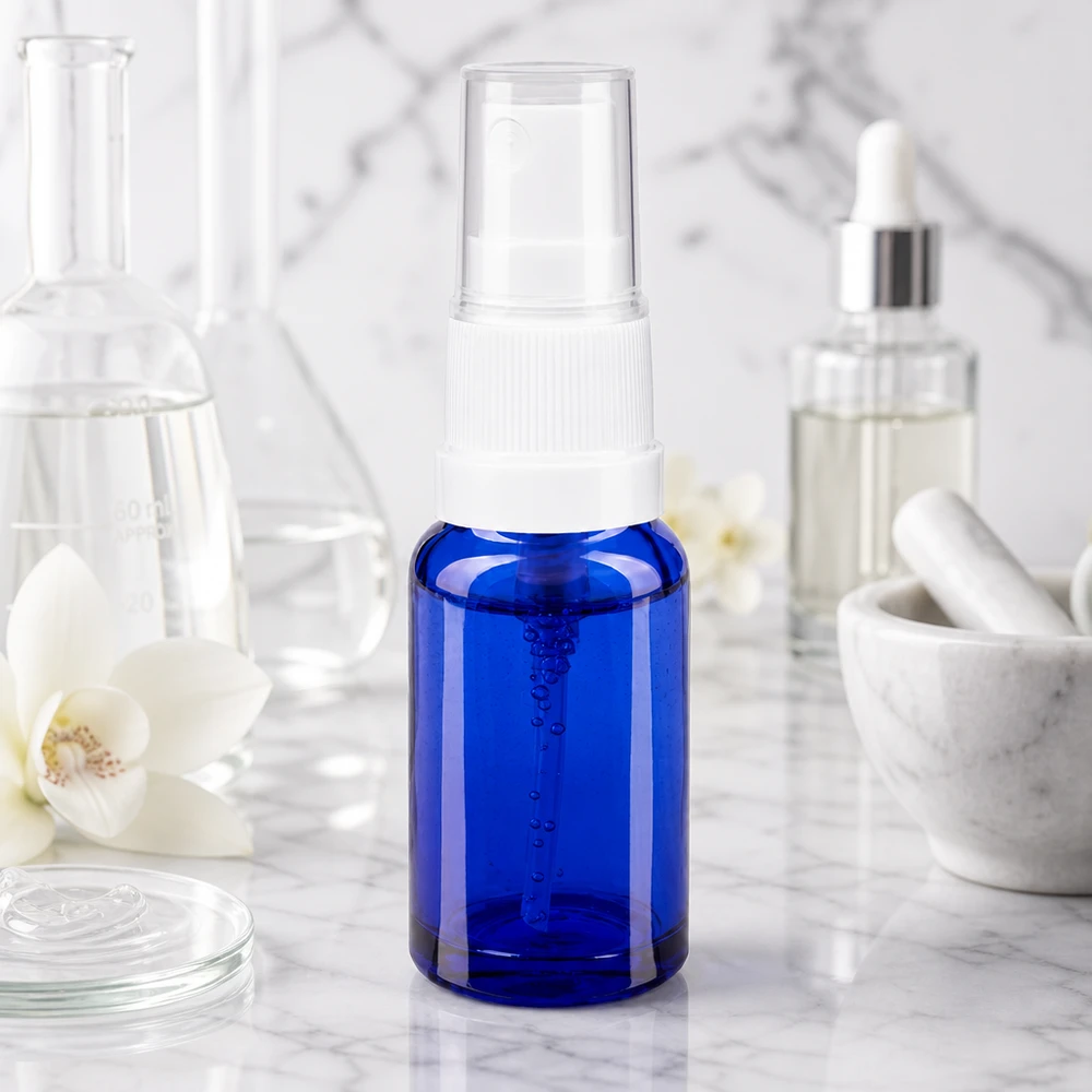 Kleine blaue Glasflasche mit Pumpzerstäuber neben Erlenmeyerkolben Mörser und Kosmetikserum