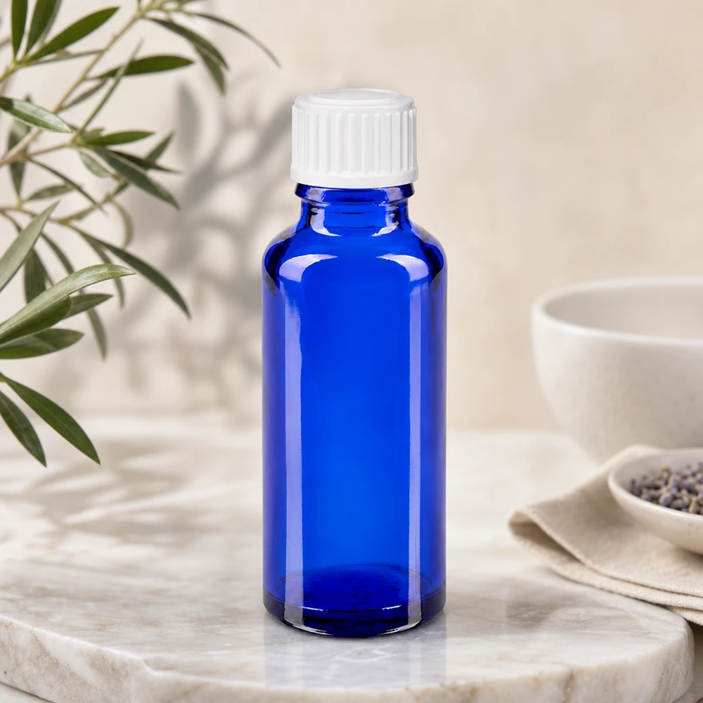 Apothekenflasche blau 30ml Schraubverschluss weiß Standard Blaue Apothekerflasche 30ml auf Marmorunterlage neben Lavendel und Eukalyptuszweigen