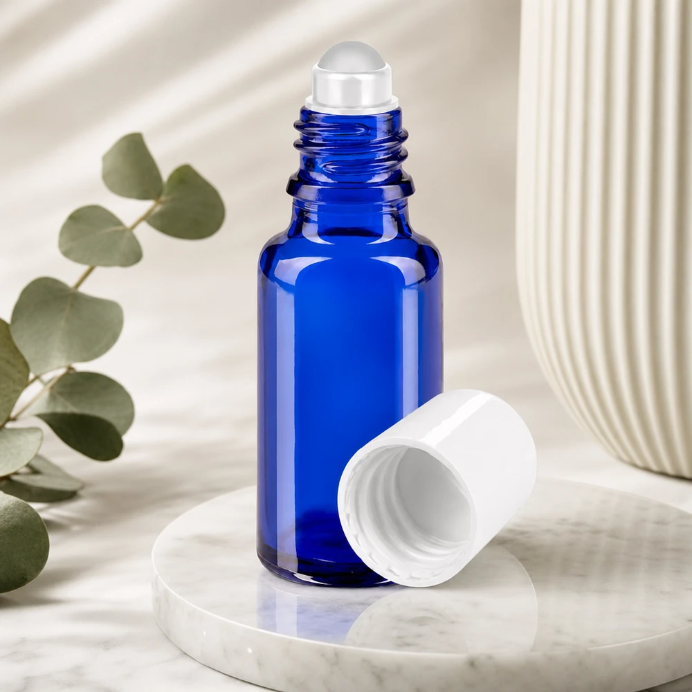 Kobaltblaue Glasflasche mit transparenter Rollkugel und weißem Verschluss neben Eukalyptuszweig