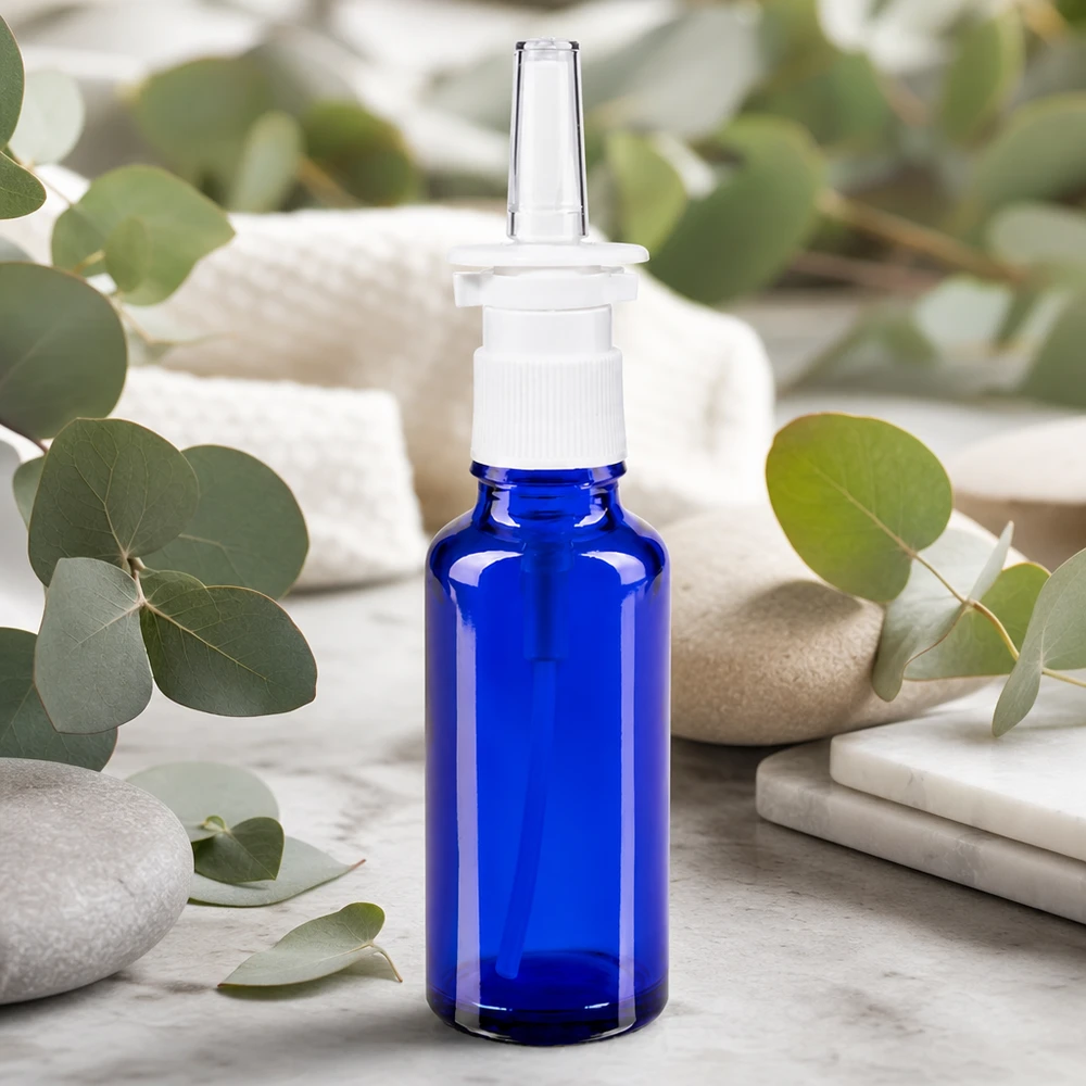 Kleine blaue Glasflasche 30ml mit Nasenapplikator auf weißem Marmor zwischen Wellness-Steinen