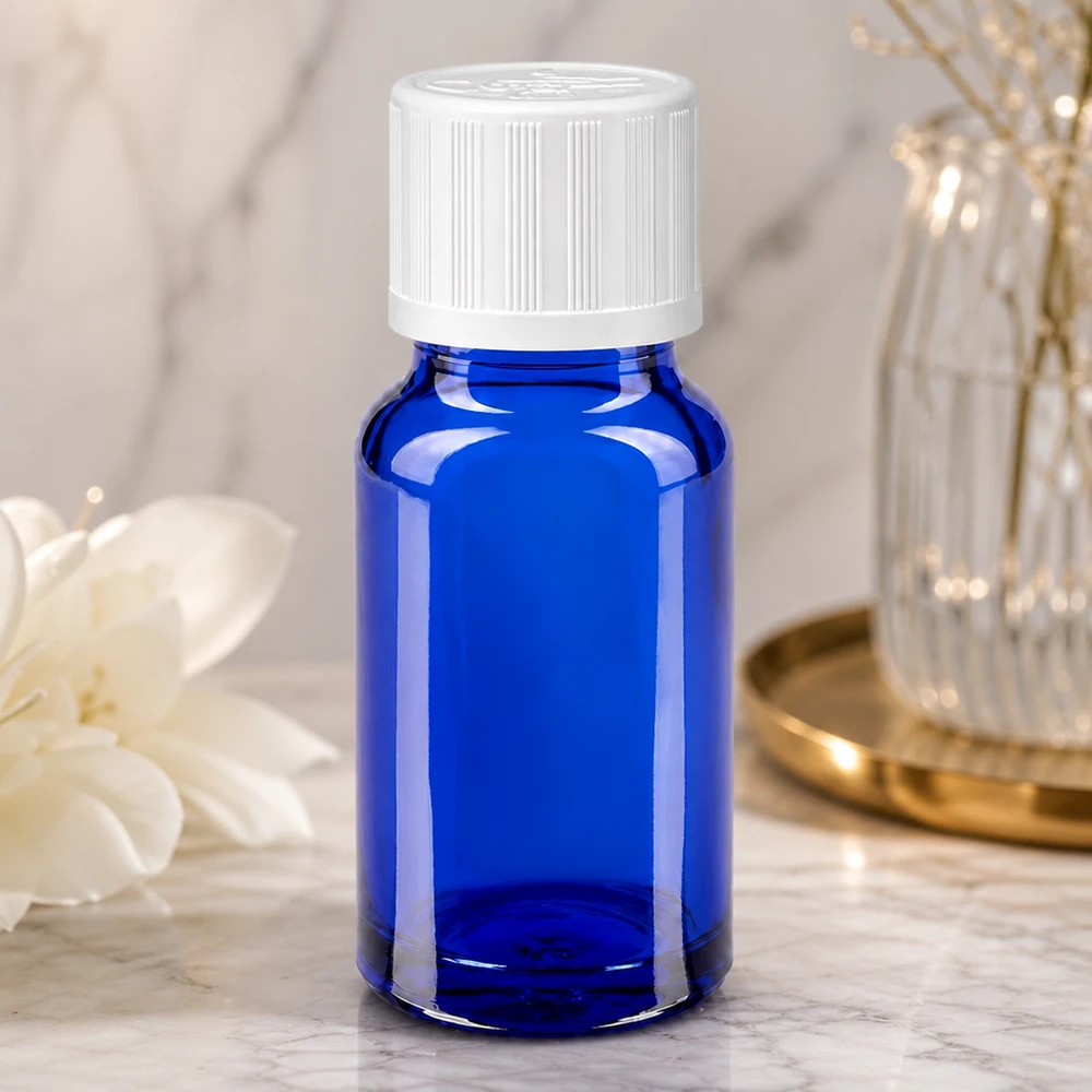 Blaue Glasflasche 10ml mit weißem Schraubverschluss neben weißer Blüte und Glasvase