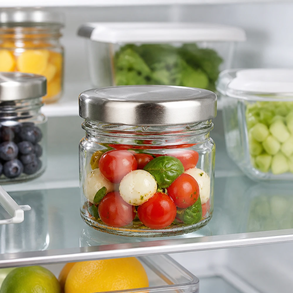 Transparentes Vorratsglas 33ml mit Edelstahl-Optik Deckel neben Obst und Gemüse im Kühlschrank