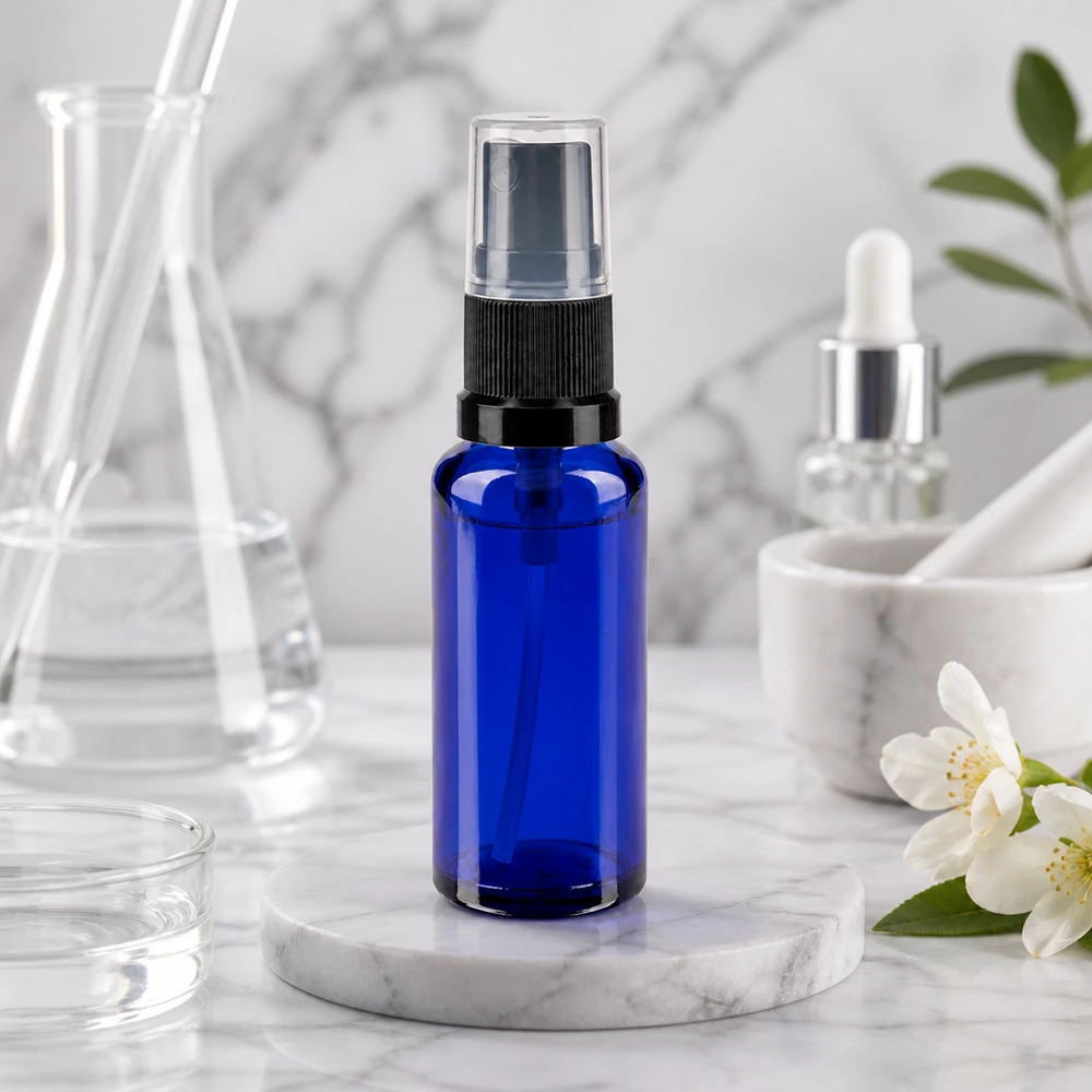 Apothekenflasche blau 30ml Sprayaufsatz schwarz Blaue Glasflasche 30ml mit Feinzerstäuber schwarz transparent neben weißen Jasminblüten