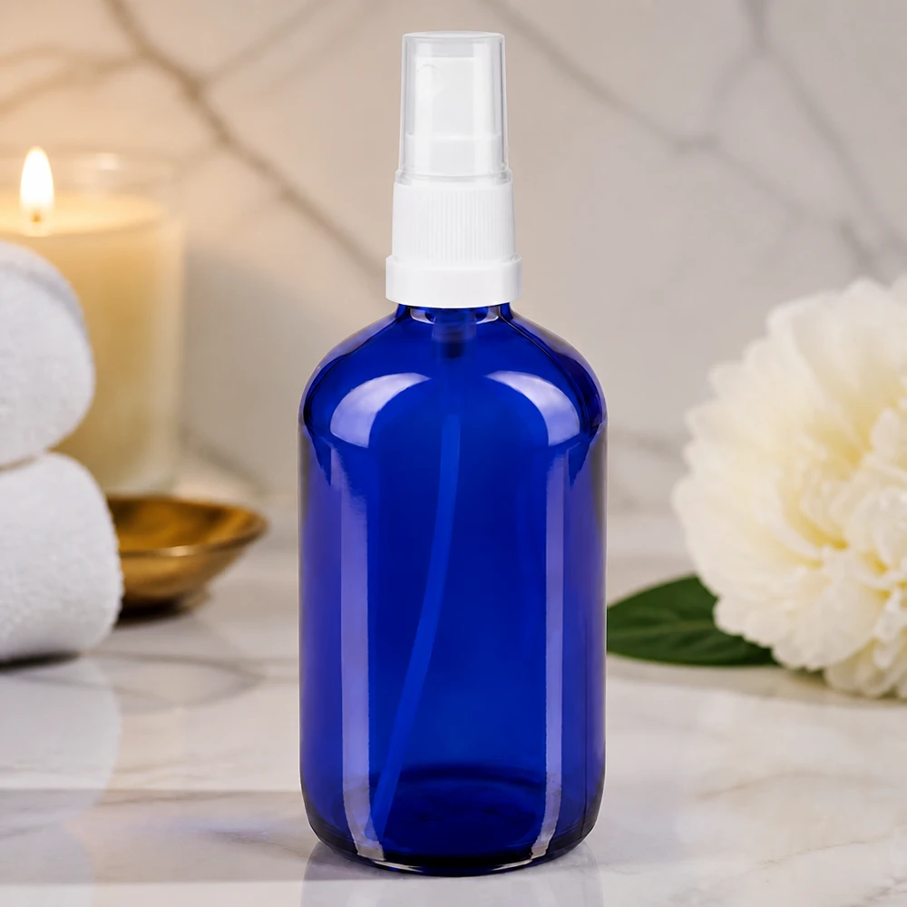 Apothekenflasche blau 100ml Sprayaufsatz weiß Kobaltblaue Glasflasche 100ml mit weißem Sprühkopf auf Marmor im Spa-Ambiente
