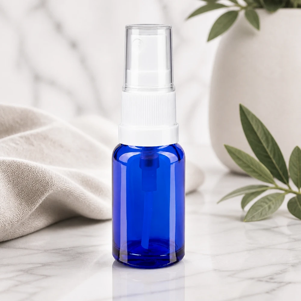 Kompakte Sprayflasche aus kobaltblauem Glas 10ml mit weißem Sprühkopf auf Marmoruntergrund